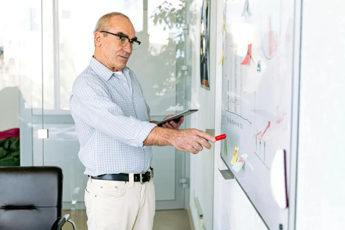 Man using a tablet and writing on a whiteboard.