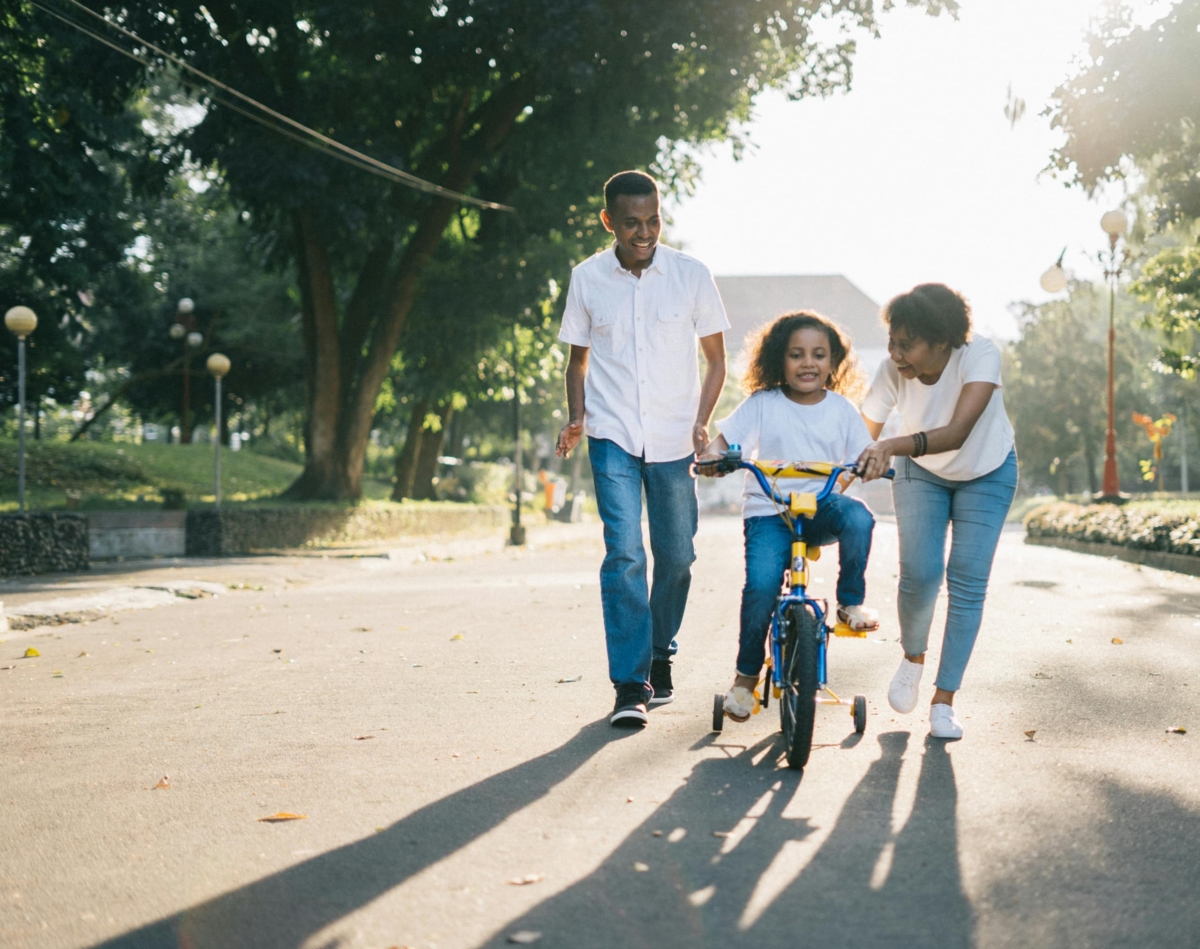 Father and mother teaching their daughter to ride a bicycle in their neighbourhood.