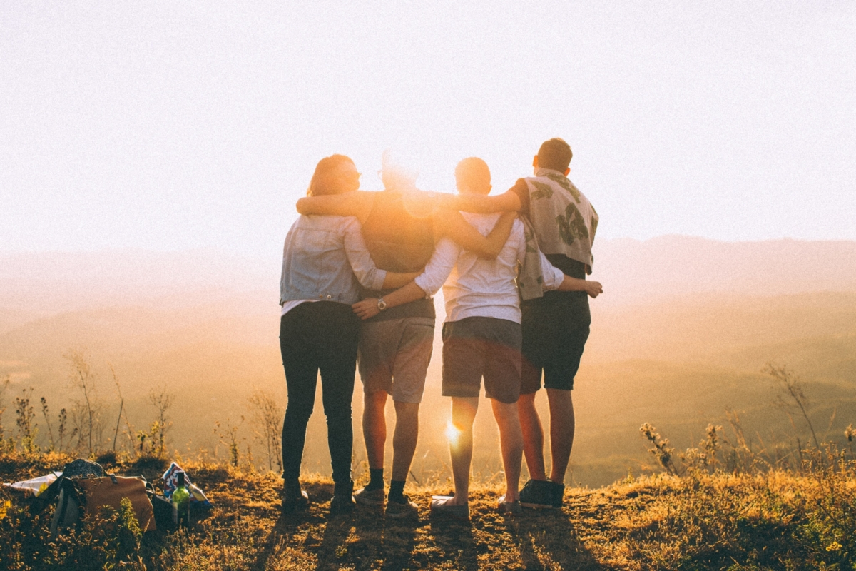Four friends embracing each other and enjoying the sunset after a hike.