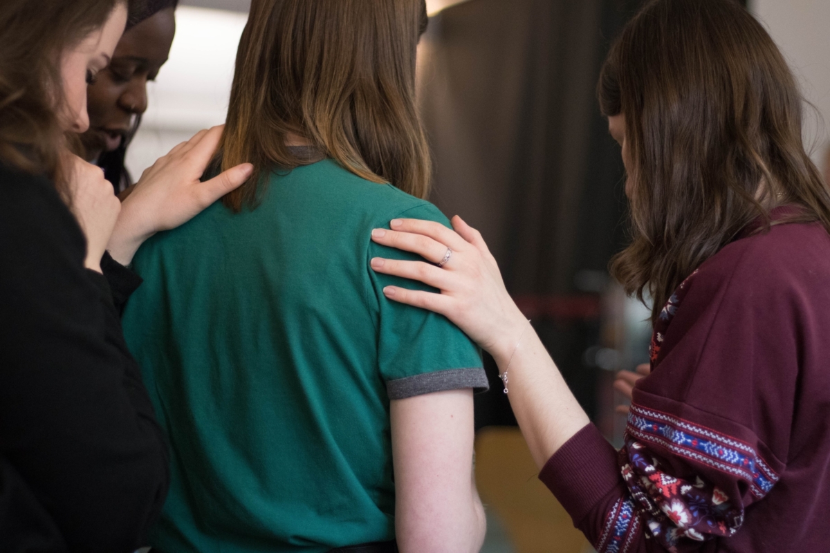 Four women looking down as they comfort each other.
