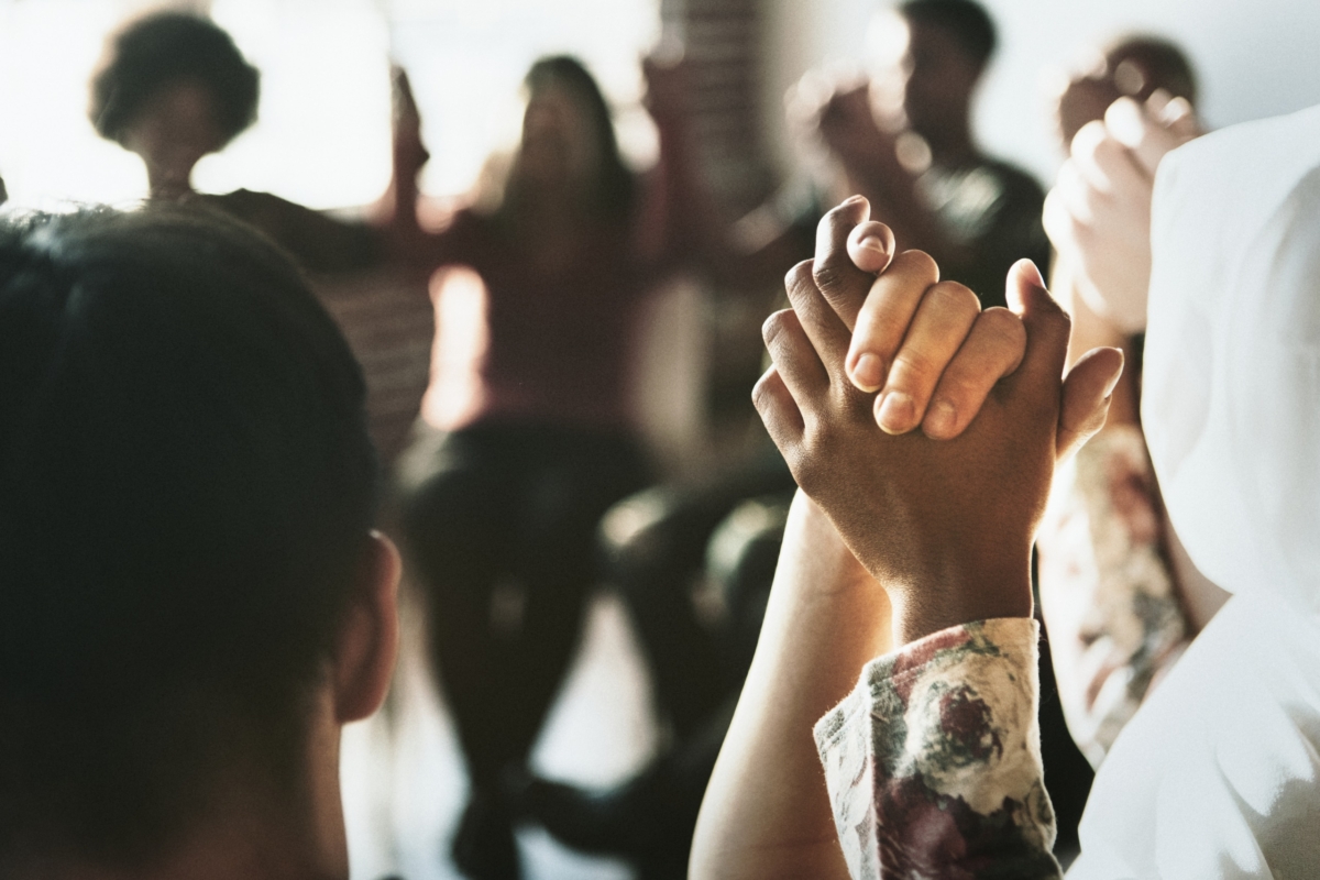 Group of people holding their hands up in the air together in a circle.