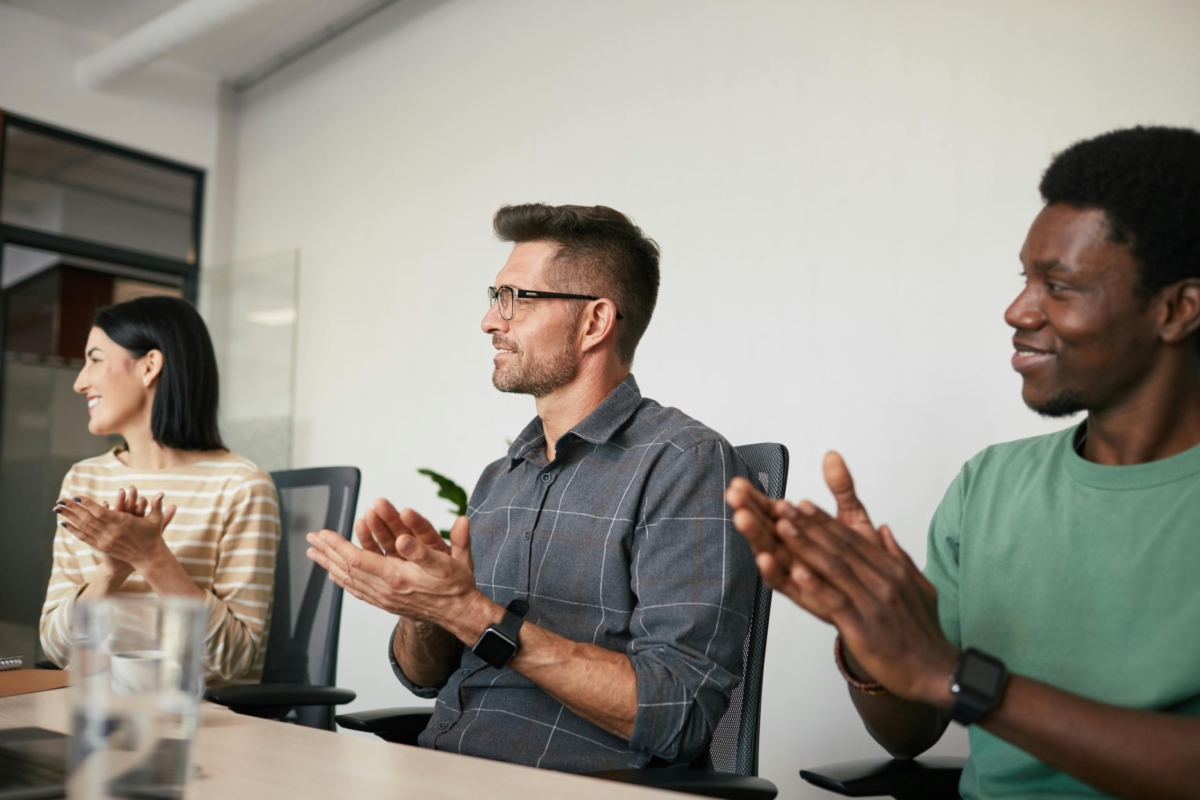 Three colleagues clapping their hands and celebrating in a meeting room.