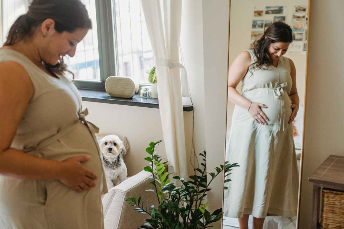 Pregnant woman admiring her baby bump through a full-length mirror.