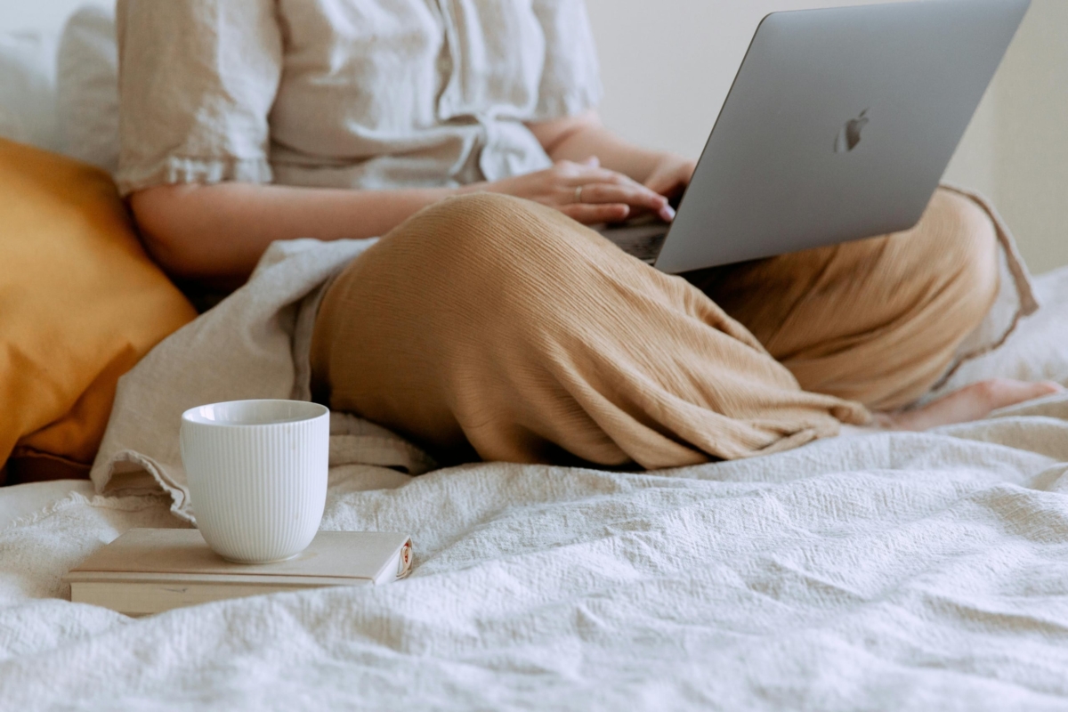 Woman on her bed working on her laptop with a cup of coffee by her side.