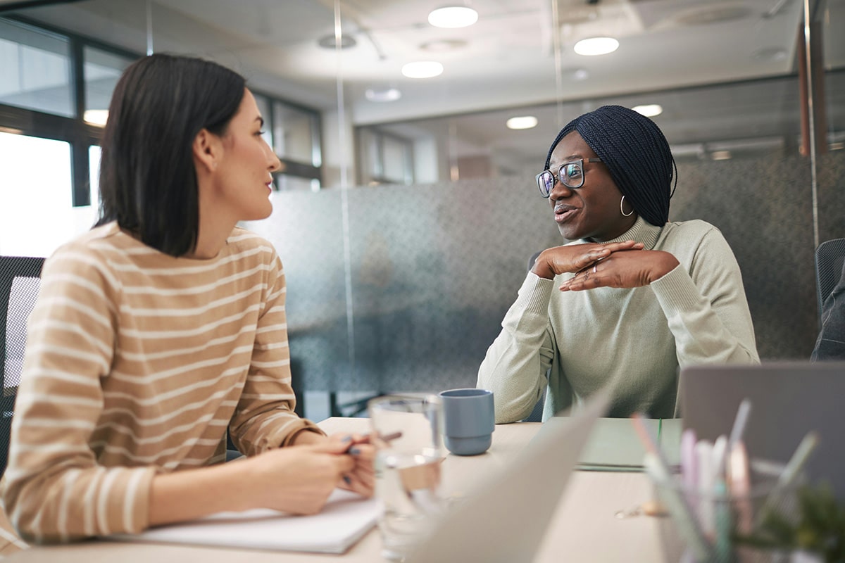 Two female colleagues chatting happily while at work in an office.