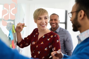Woman smiling at her colleague while writing a note on a whiteboard during a meeting.