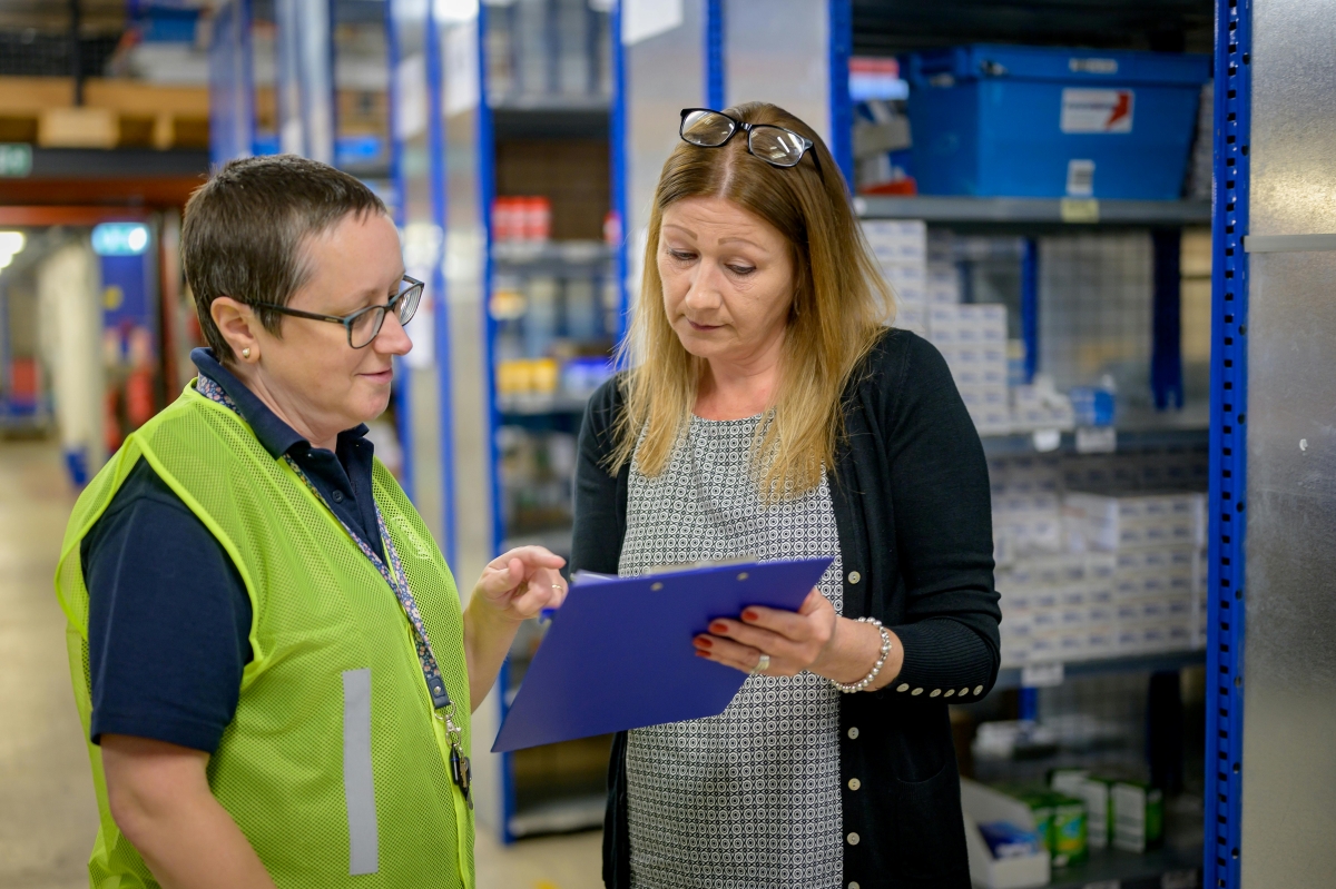 Manager and employee looking over a clipboard and talking in a warehouse.